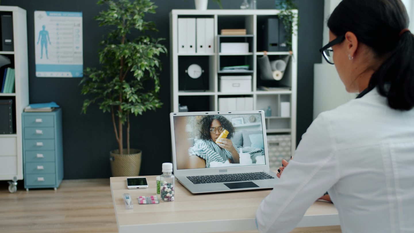 Doctor on telehealth call with patient holding yellow pill bottle.