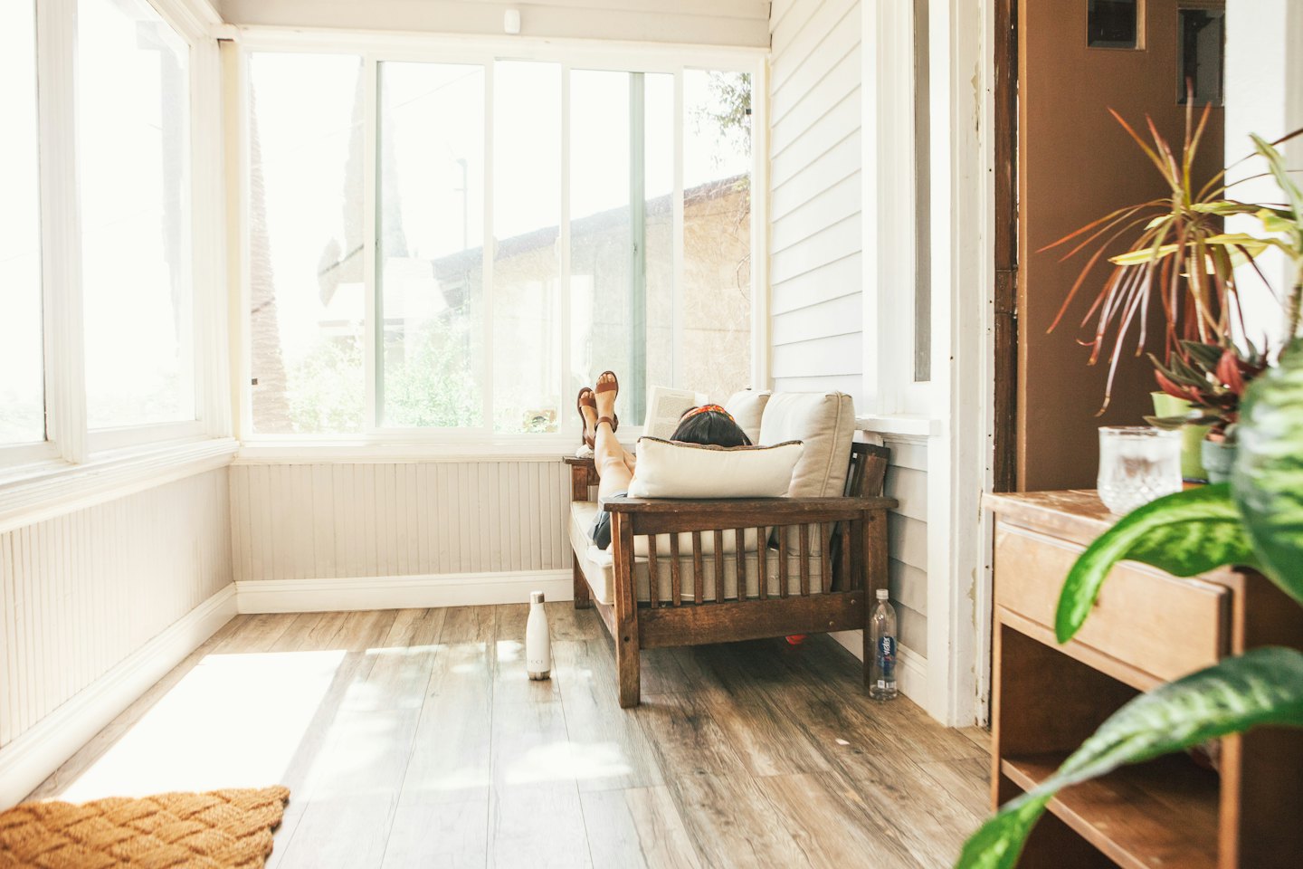 Person relaxing on a sofa in a sunlit room with a newspaper.